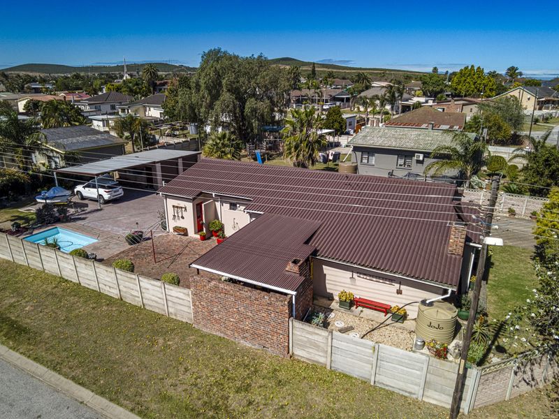 Aerial view of a residential property featuring a corrugated metal roof, swimming pool, carport, and perimeter boundary walling in a suburban setting.