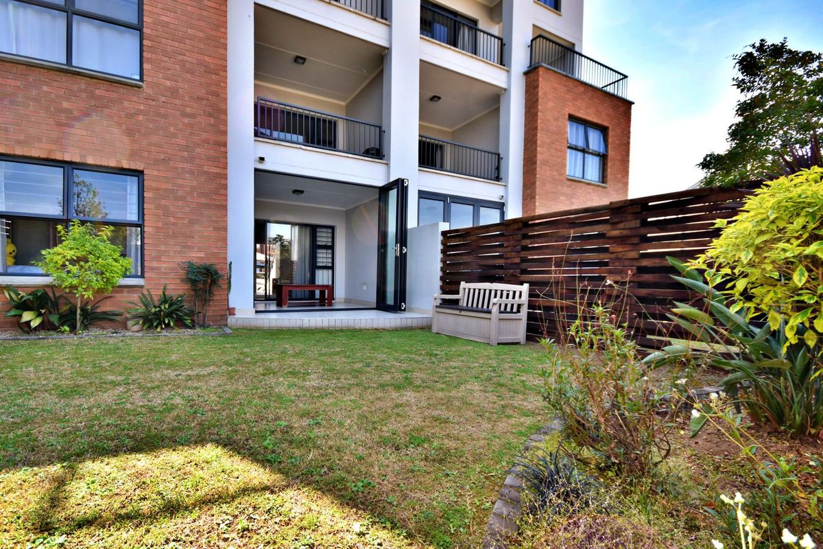 Rear view of an apartment building featuring a private garden, timber fencing, and a tiled patio accessible through modern bi-fold doors.