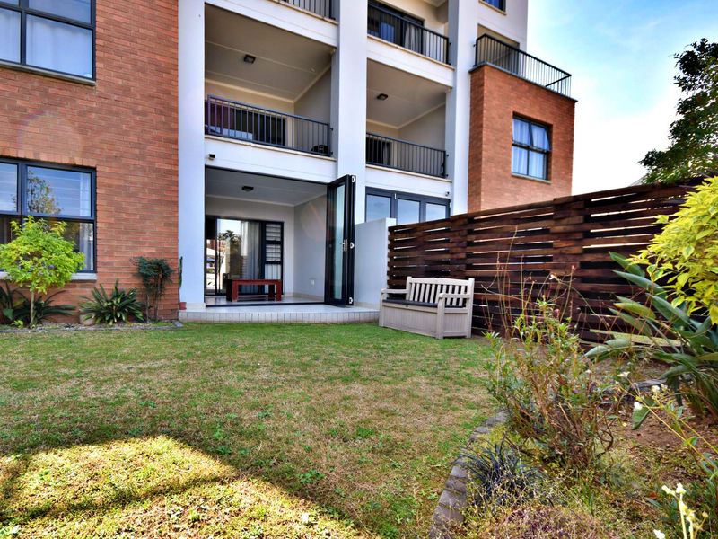 Rear view of an apartment building featuring a private garden, timber fencing, and a tiled patio accessible through modern bi-fold doors.