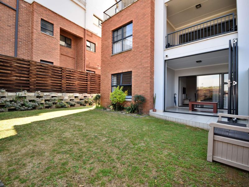 Rear view of the apartment featuring a private garden, brick facade, tiled patio area, and access to the living space via large sliding doors.