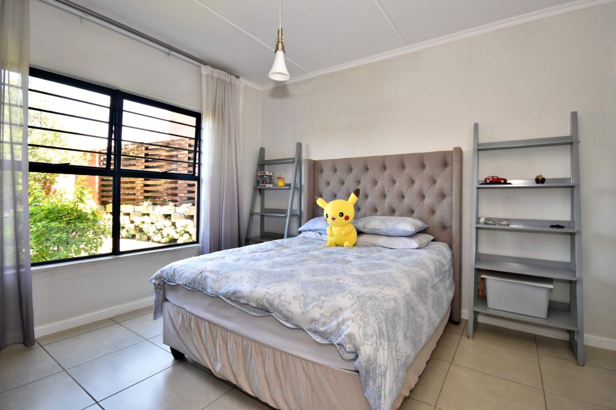 A well-lit bedroom featuring tiled flooring, a large window with security bars, and a neutral color palette.