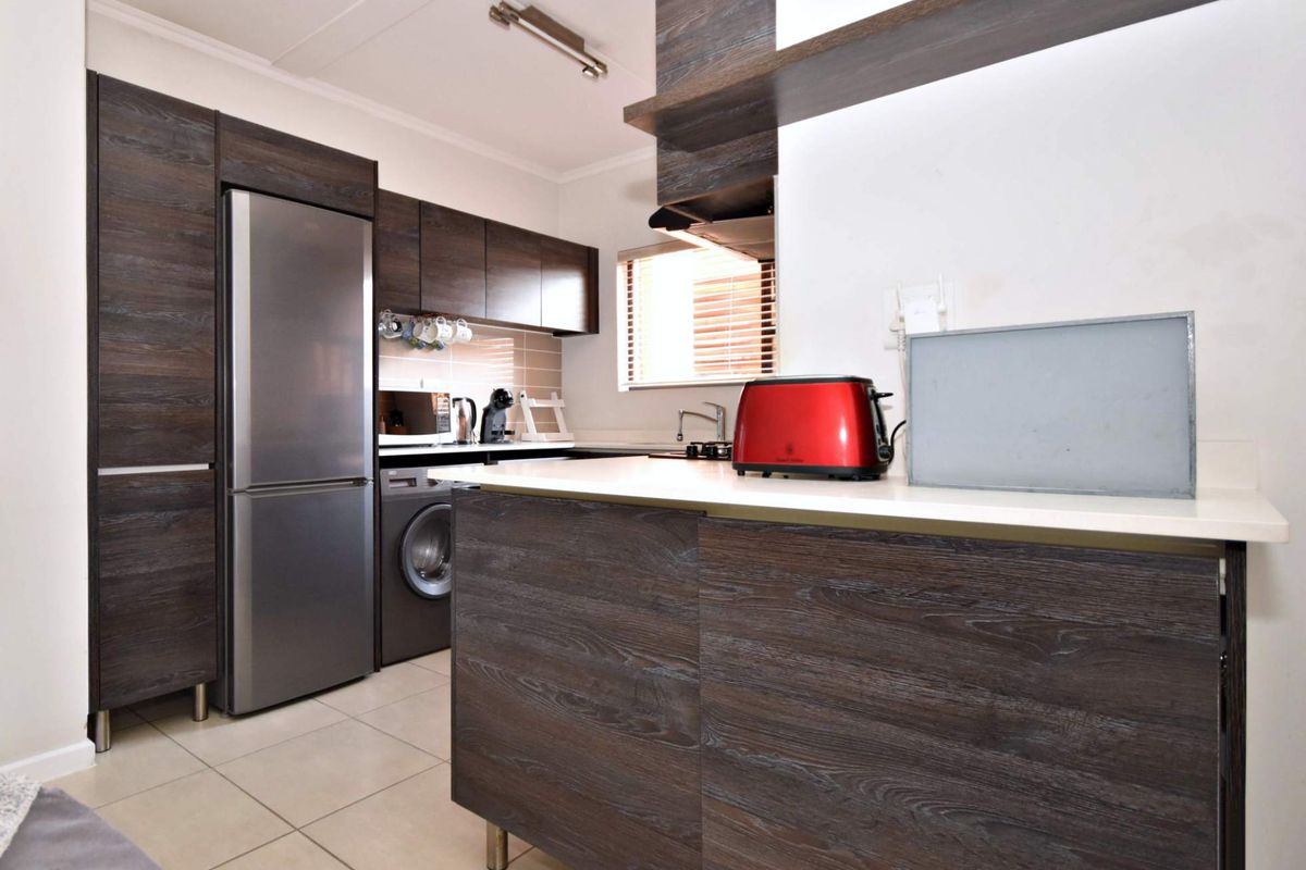 Modern kitchen featuring dark wood-grain cabinetry, stone countertops, integrated appliances, and neutral tiled flooring in a compact, functional layout.