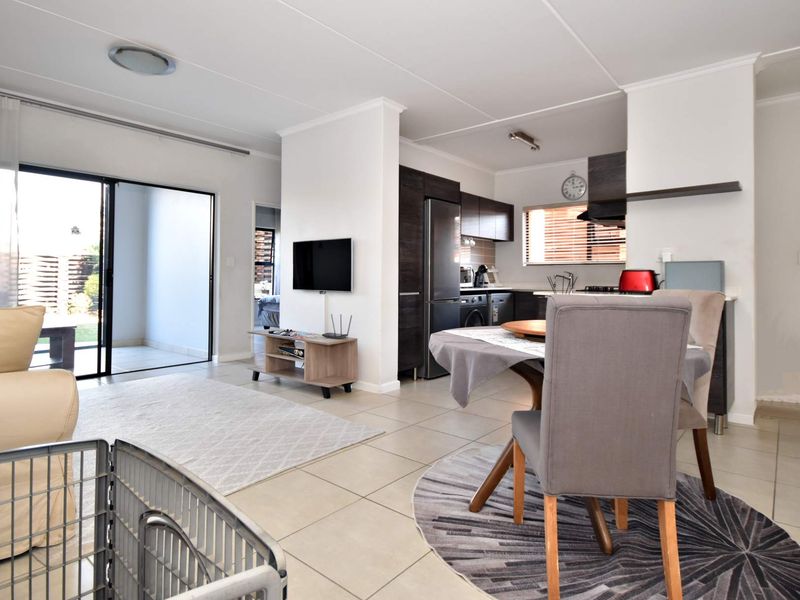 An open-plan living and dining area featuring tiled floors, a modern kitchen with built-in cabinetry, and direct access to an outdoor patio.