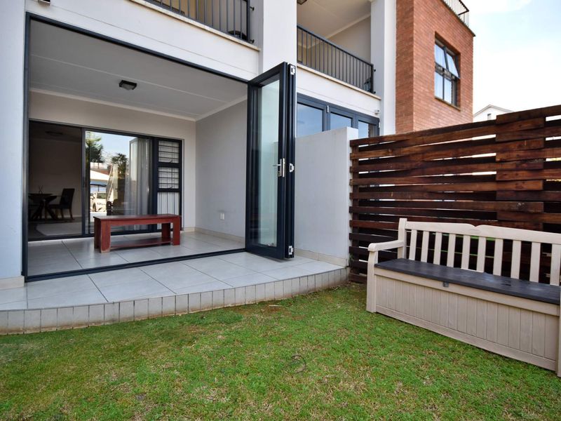 A ground floor apartment featuring a tiled patio with bi-fold doors, leading to a private garden area with a timber privacy screen.