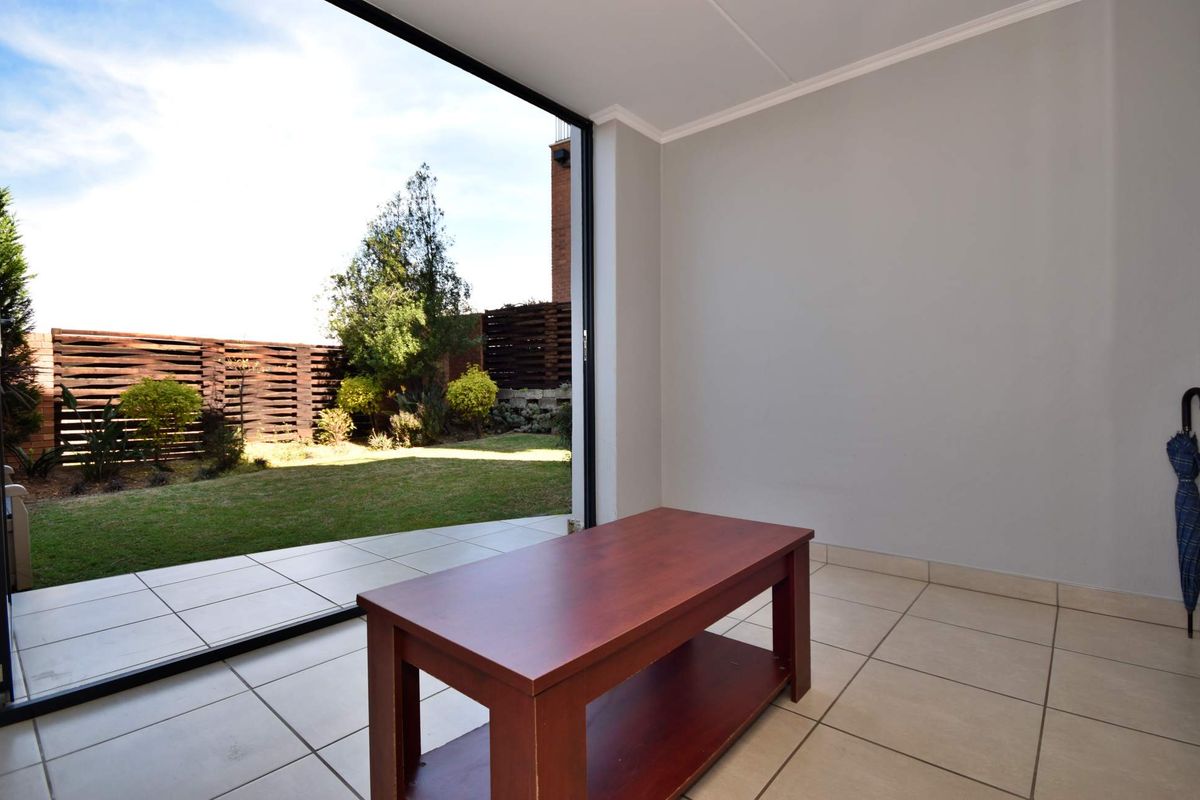 Bright living area featuring large sliding glass doors that open onto a private garden, finished with neutral ceramic floor tiles.
