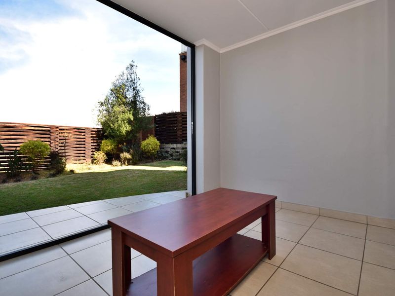 Bright living area featuring large sliding glass doors that open onto a private garden, finished with neutral ceramic floor tiles.