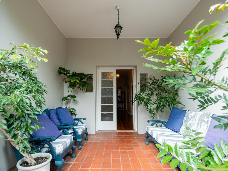 A covered patio area featuring terracotta tile flooring and a classic multi-pane glass entrance door, providing a welcoming outdoor transition space.