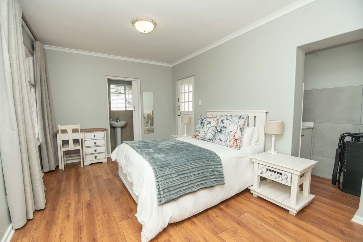 A well-maintained bedroom featuring laminate flooring, neutral wall tones, and an attached en-suite bathroom with a pedestal sink.