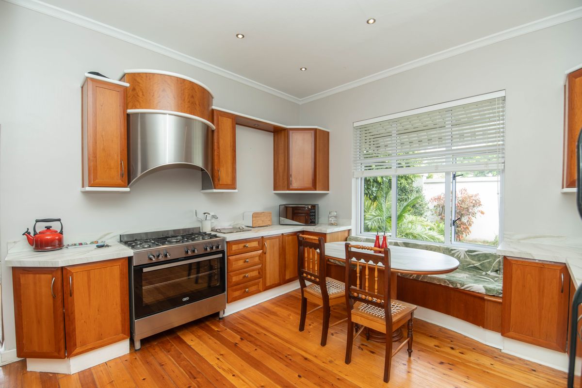 A well-maintained kitchen featuring warm timber cabinetry, stainless steel gas stove, marble-look countertops, and a cozy built-in window seat overlooking the garden.