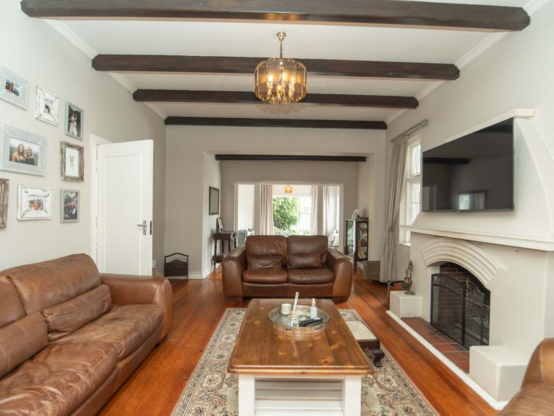 A cozy living room featuring exposed timber ceiling beams, hardwood flooring, and a classic fireplace with a decorative mantel.