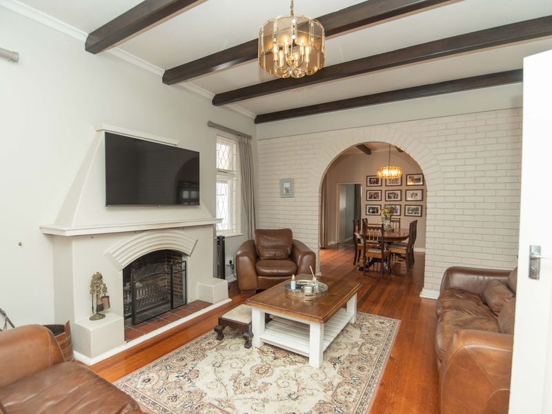 Spacious living room featuring exposed timber ceiling beams, a classic masonry fireplace, and a charming brick archway leading to the dining area.