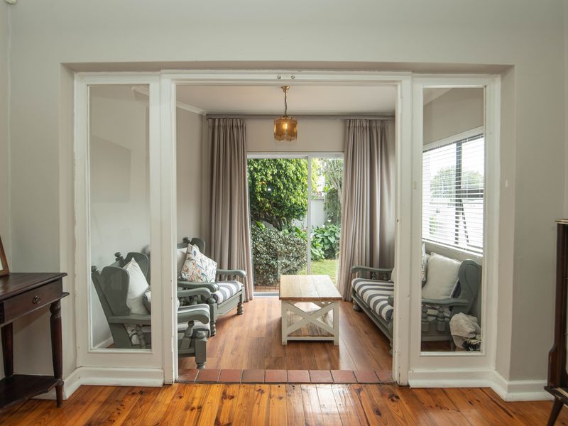 A bright living room featuring polished hardwood floors, glass panel double doors, and a sliding door providing direct access to the garden.