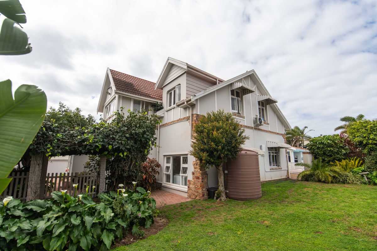 Rear view of a multi-story house featuring timber cladding, stone accents, a tiled roof, and a private garden with a water tank and pergola.