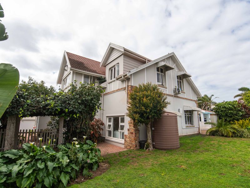 Rear view of a multi-story house featuring timber cladding, stone accents, a tiled roof, and a private garden with a water tank and pergola.
