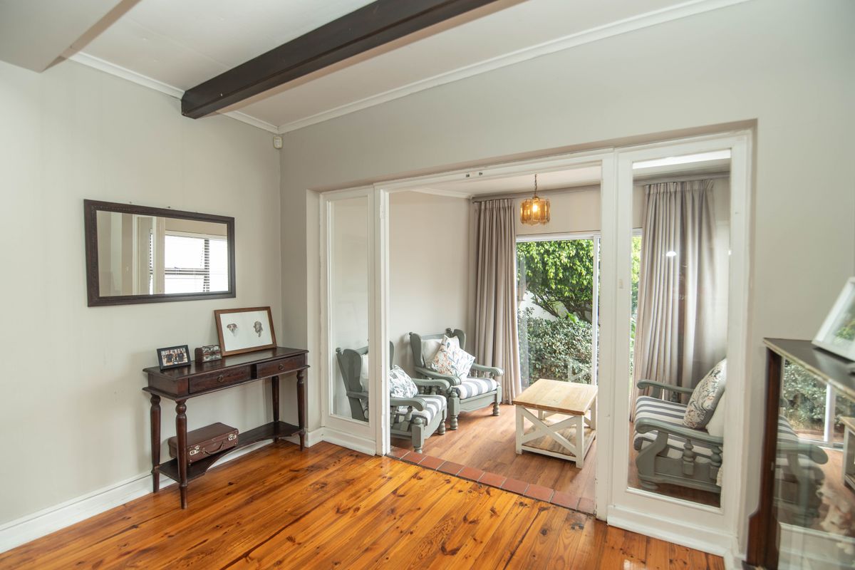 A bright living area featuring polished hardwood floors, exposed timber ceiling beams, and large sliding glass doors leading to an outdoor patio space.