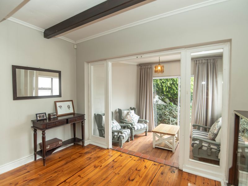 A bright living area featuring polished hardwood floors, exposed timber ceiling beams, and large sliding glass doors leading to an outdoor patio space.