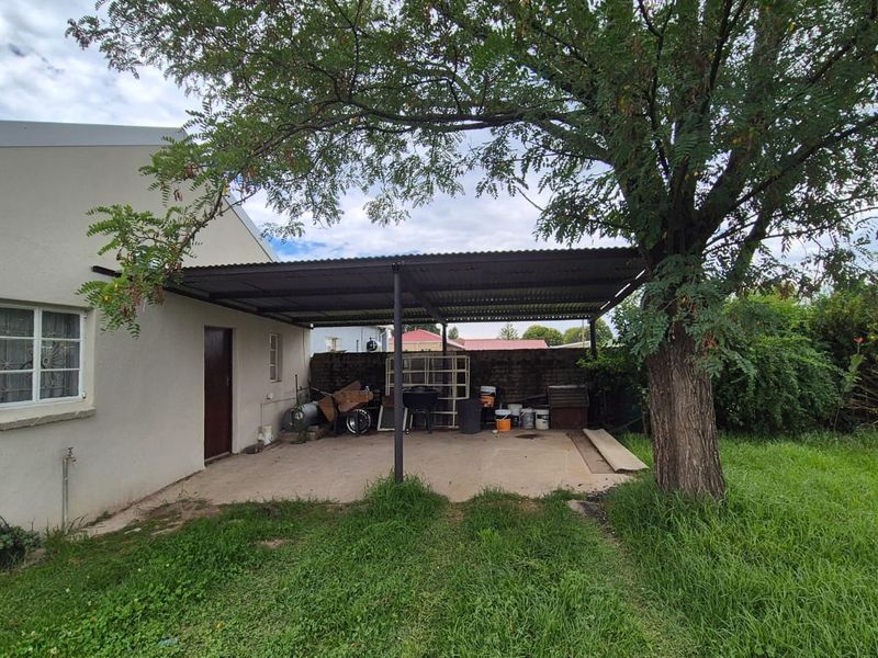 A covered outdoor patio area featuring a corrugated metal roof, concrete flooring, and direct access to the rear garden space.