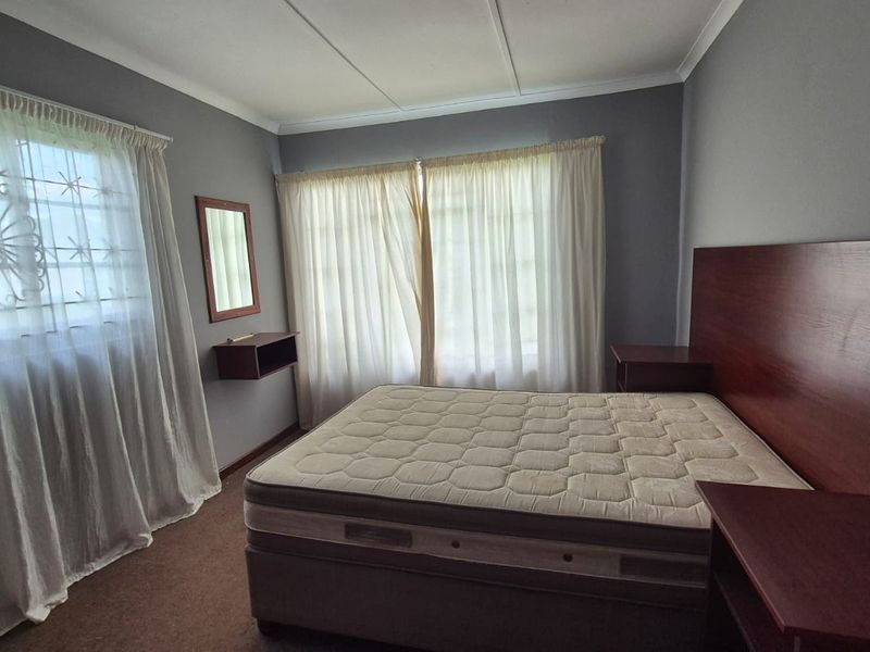 A bedroom featuring a built-in headboard with integrated bedside tables, a wall-mounted shelf, and windows fitted with security bars.
