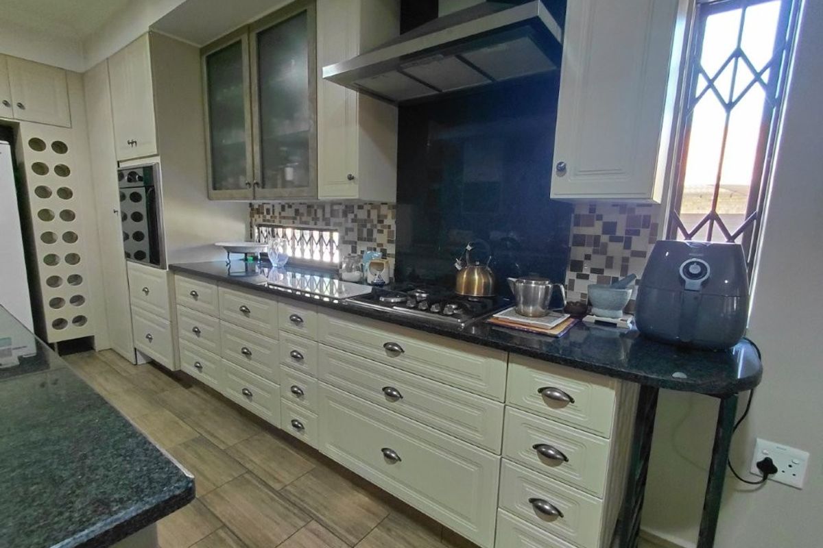 A well-appointed kitchen featuring cream cabinetry, granite countertops, a gas hob with extractor fan, and a decorative mosaic tile backsplash.