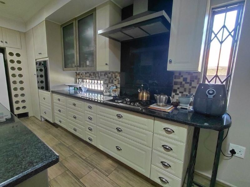 A well-appointed kitchen featuring cream cabinetry, granite countertops, a gas hob with extractor fan, and a decorative mosaic tile backsplash.