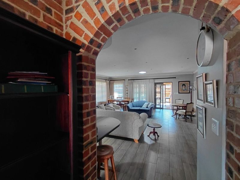 Spacious open-plan living area featuring an exposed brick archway, tiled flooring, recessed lighting, and a skylight, with direct access to the outdoor patio.