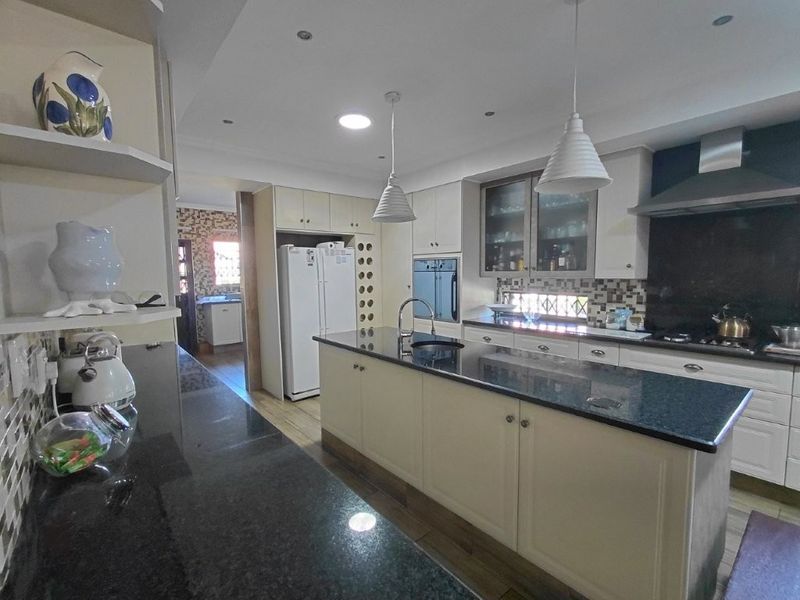 Spacious kitchen featuring a large central island with granite countertops, built-in oven, gas hob, extractor fan, and ample cabinetry for storage.