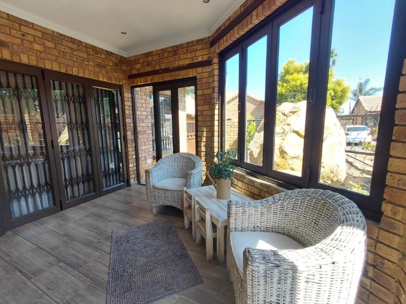 A bright, enclosed patio featuring exposed brick walls, wood-look tiled flooring, and large aluminium-framed windows providing ample natural light.