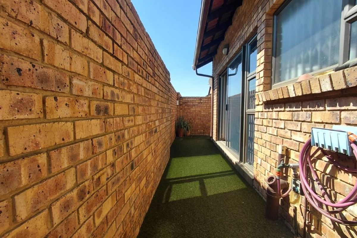 A narrow side passage featuring face brick walls, artificial grass flooring, and access to the home via a sliding glass door.