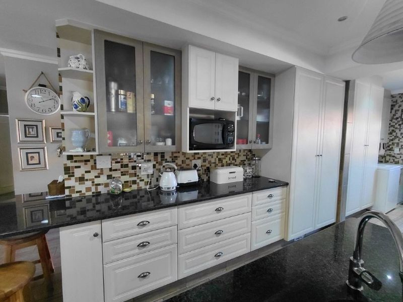 Modern kitchen featuring shaker-style cabinetry, granite countertops, a mosaic tile backsplash, and integrated appliances, offering a clean and functional culinary space.