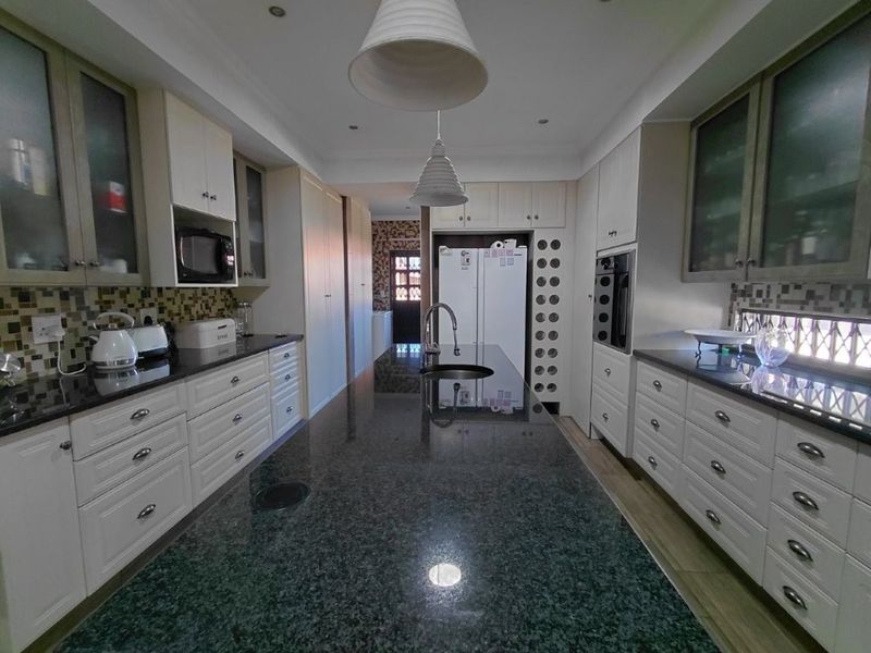 Spacious kitchen featuring a large granite-topped island, extensive cabinetry, built-in appliances, and a decorative mosaic tile backsplash.