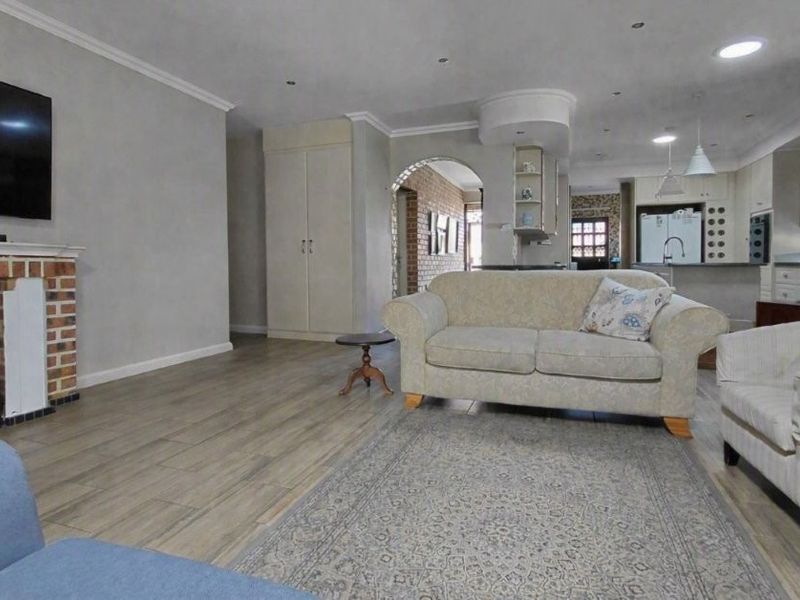 Spacious open-plan living area featuring a brick fireplace, wood-look tile flooring, and a seamless transition into the kitchen with island seating.