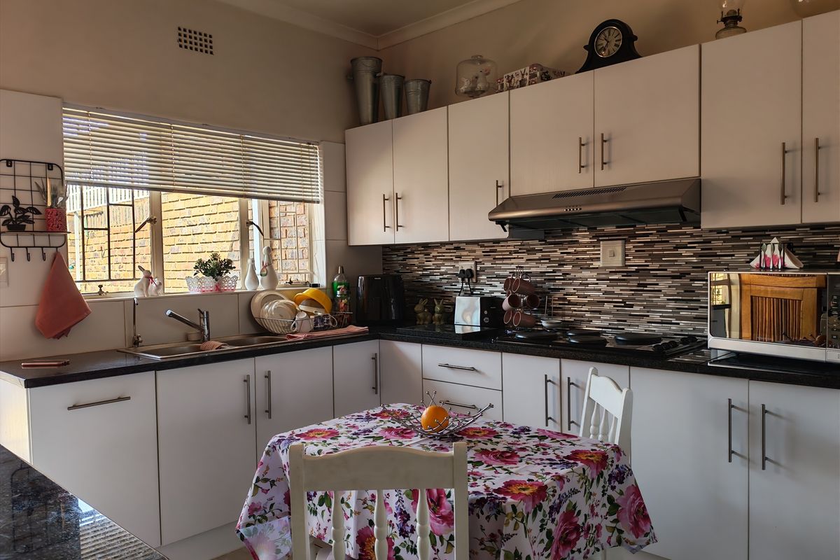 A functional kitchen featuring white cabinetry, dark countertops, a mosaic tiled backsplash, and a built-in hob with an extractor fan.