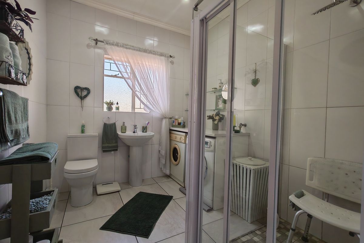 A functional bathroom featuring a pedestal basin, toilet, and a glass-enclosed shower with a rain shower head, including integrated laundry appliance space.