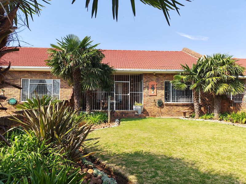 A well-maintained townhouse exterior featuring a classic face brick facade, tiled roof, and established garden with security features on windows and doors.