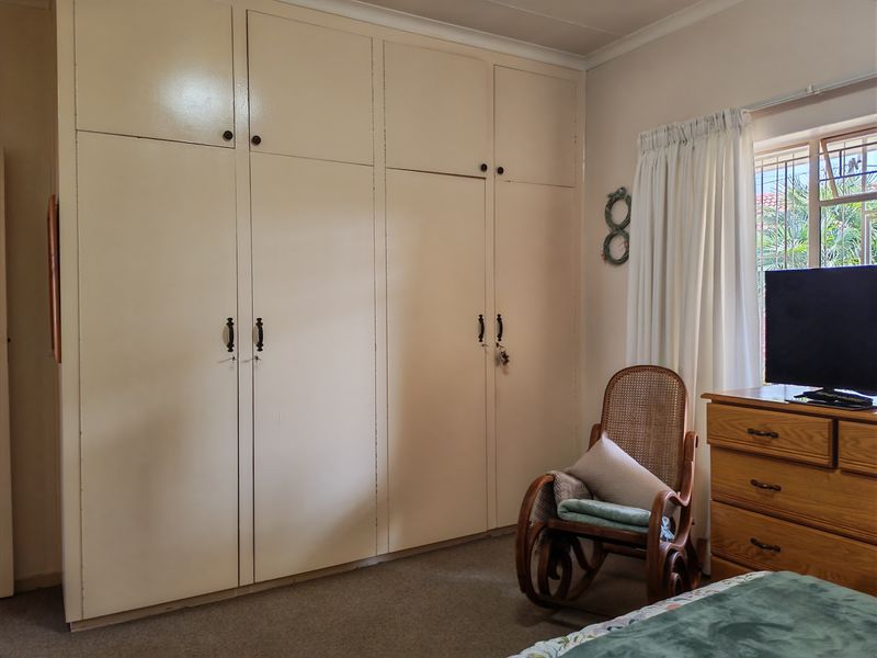 A bedroom featuring floor-to-ceiling built-in cupboards and a window with security bars, offering a functional space with potential for modern updates.
