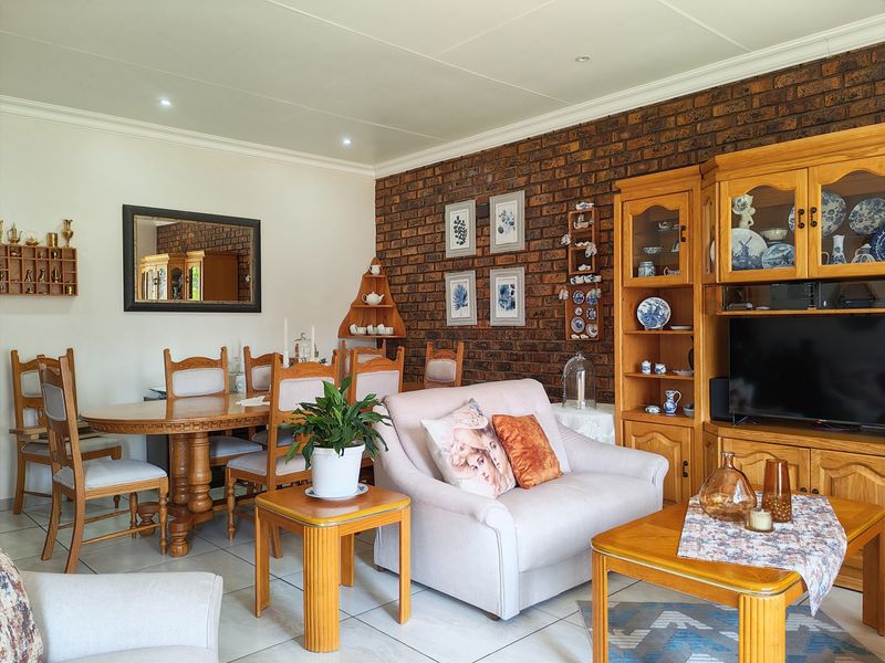 An open-plan living and dining area featuring a prominent exposed brick wall, tiled flooring, and recessed ceiling lighting.