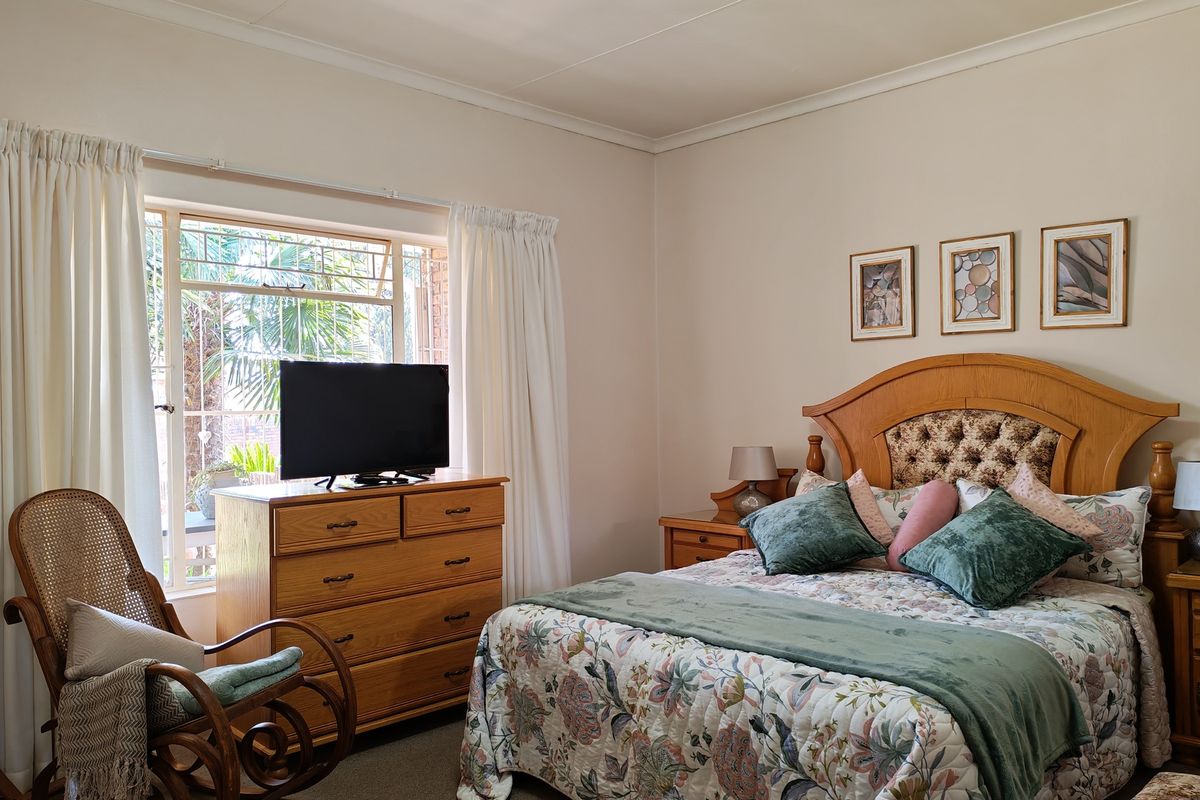 A well-maintained bedroom featuring neutral walls, coving, and a window fitted with security bars, offering a comfortable and functional living space.