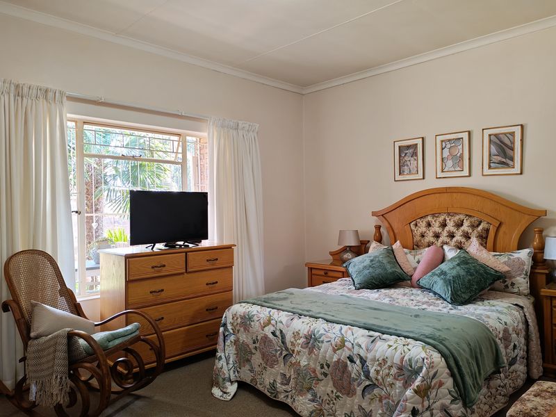 A well-maintained bedroom featuring neutral walls, coving, and a window fitted with security bars, offering a comfortable and functional living space.