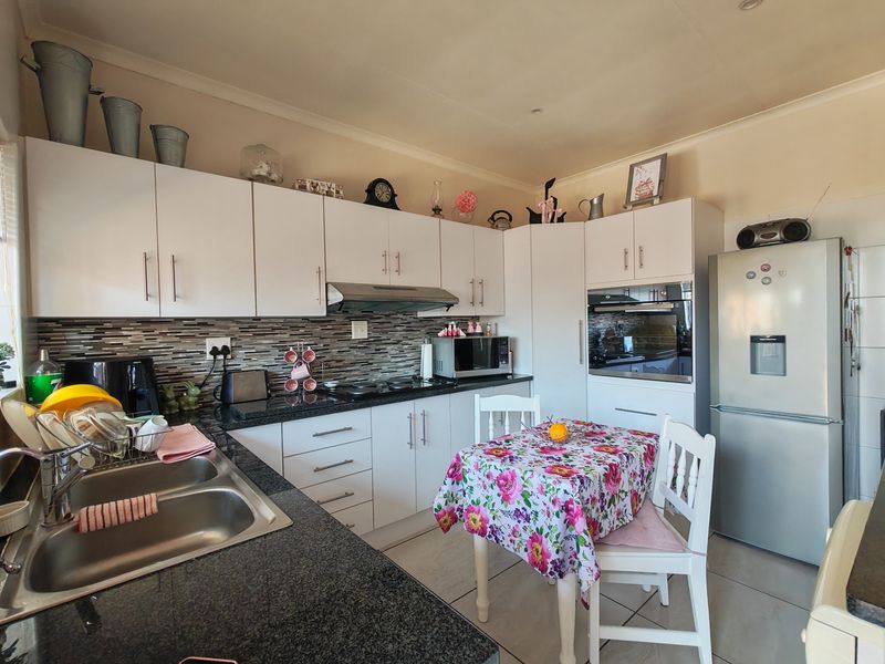 A functional kitchen featuring white cabinetry, granite countertops, a mosaic tile backsplash, and integrated appliances including an oven and hob.
