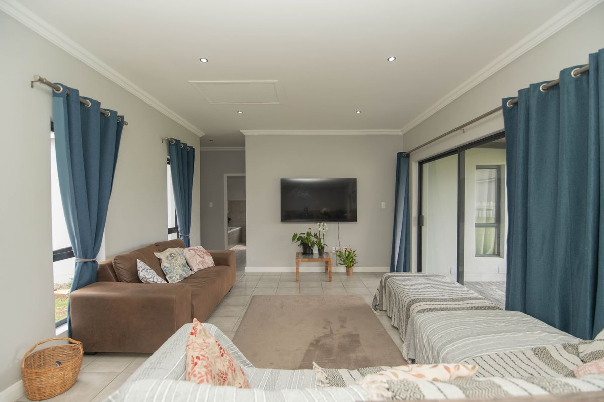 A bright, open-plan living room featuring tiled floors, recessed lighting, and large sliding glass doors that provide access to the outdoor area.
