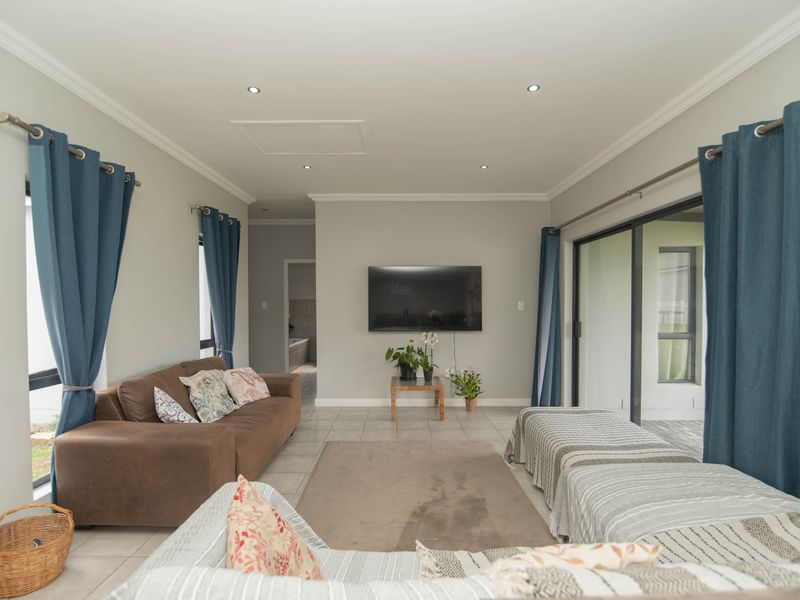 A bright, open-plan living room featuring tiled floors, recessed lighting, and large sliding glass doors that provide access to the outdoor area.