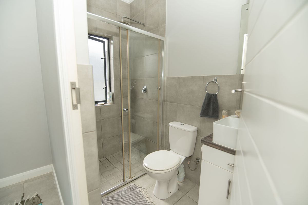 A modern bathroom featuring a glass-enclosed shower, a white toilet, and a vanity unit with a basin, finished with neutral wall and floor tiles.