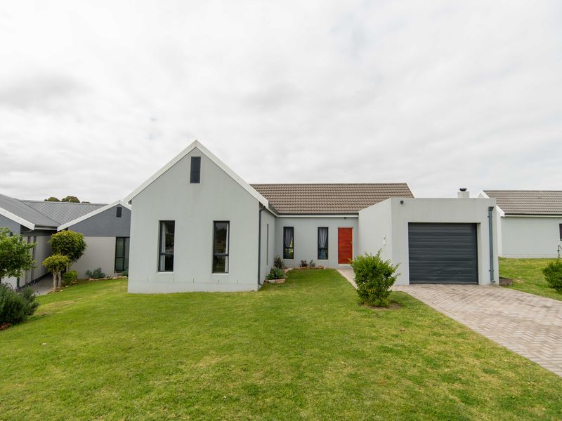 A modern single-story residential home featuring a grey rendered facade, tiled roof, single garage, and a paved driveway set within a landscaped garden.