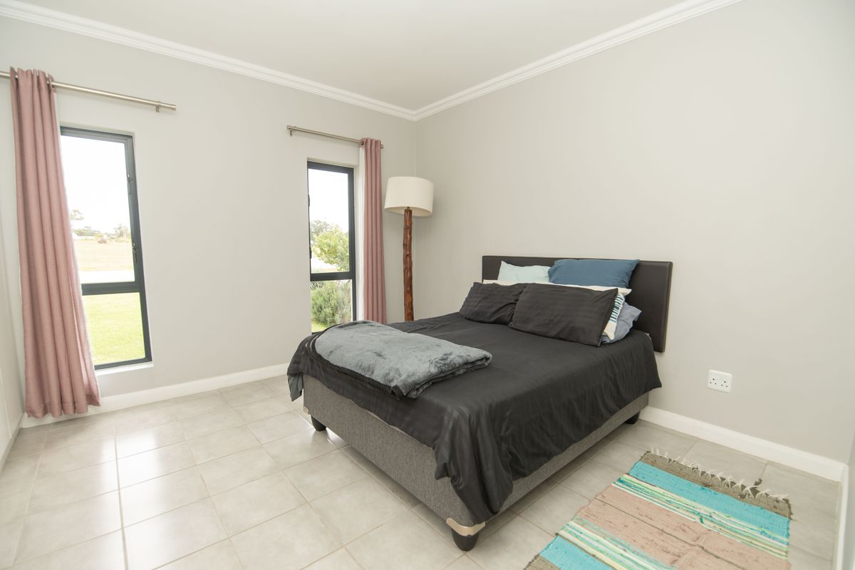 A well-maintained bedroom featuring neutral wall tones, tiled flooring, crown molding, and large aluminium-framed windows providing natural light.