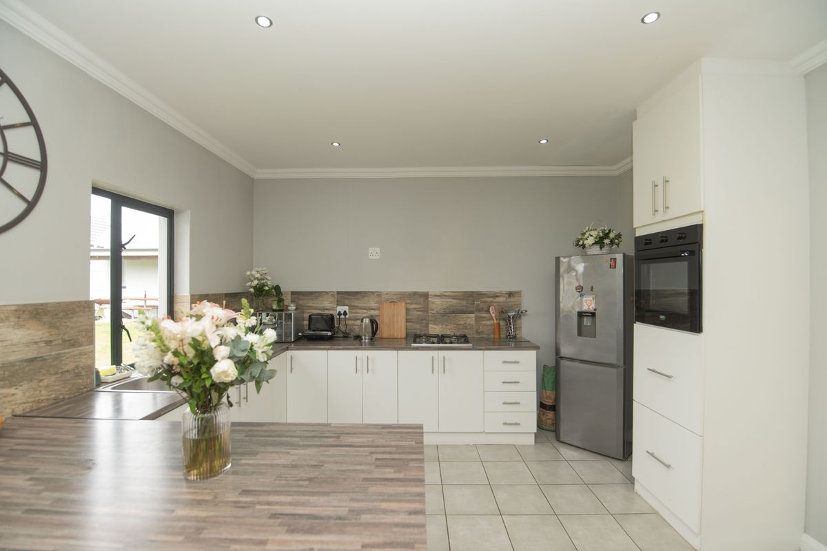Modern kitchen featuring white cabinetry, wood-look laminate countertops, tiled backsplash, built-in oven, gas hob, and tiled flooring with recessed lighting.