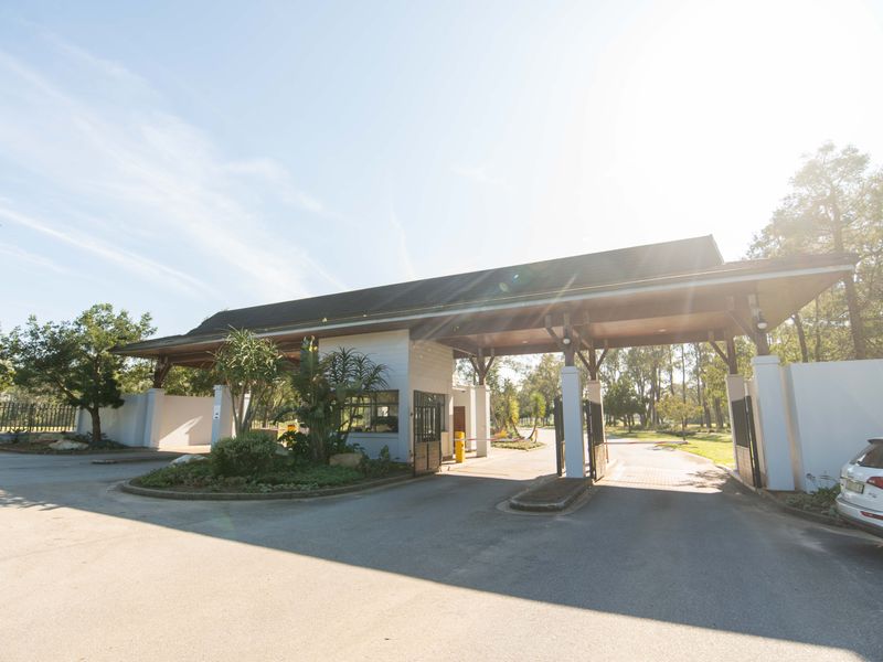 A well-maintained security gatehouse entrance featuring a timber roof structure, paved driveway, and controlled access boom gate.