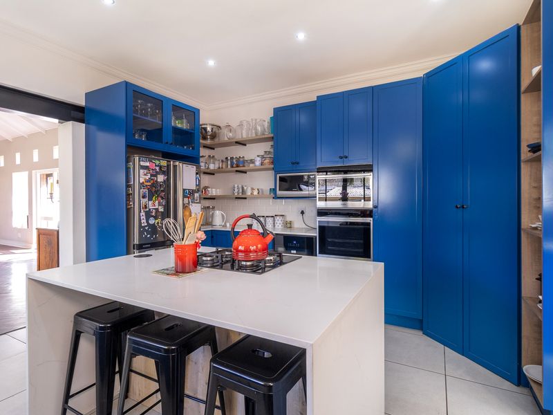 Modern kitchen featuring vibrant blue cabinetry, a central island with a stone countertop, built-in appliances, and sleek tiled flooring.