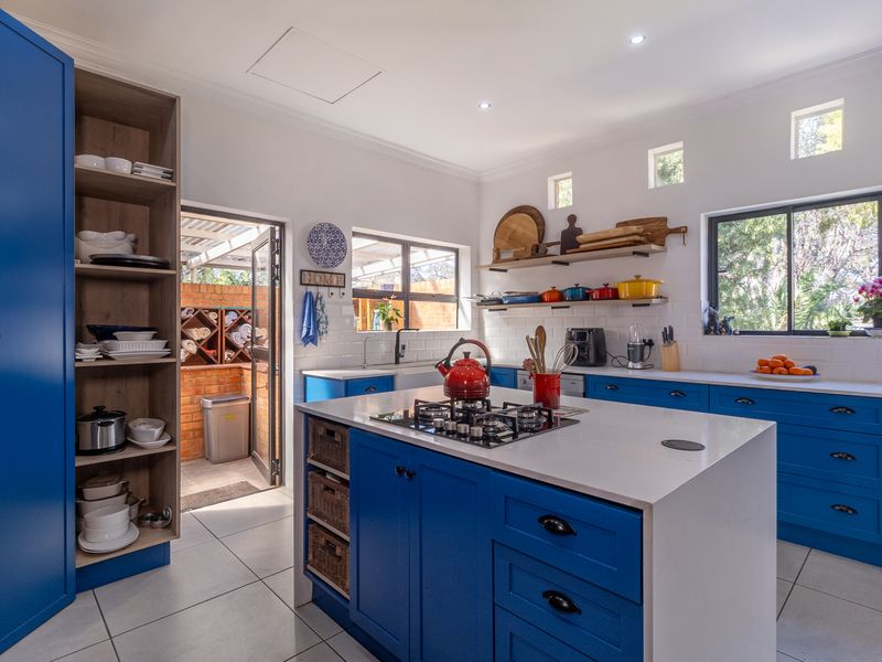 Modern kitchen featuring vibrant blue cabinetry, a central island with a gas hob, white stone countertops, subway tile backsplash, and open shelving.