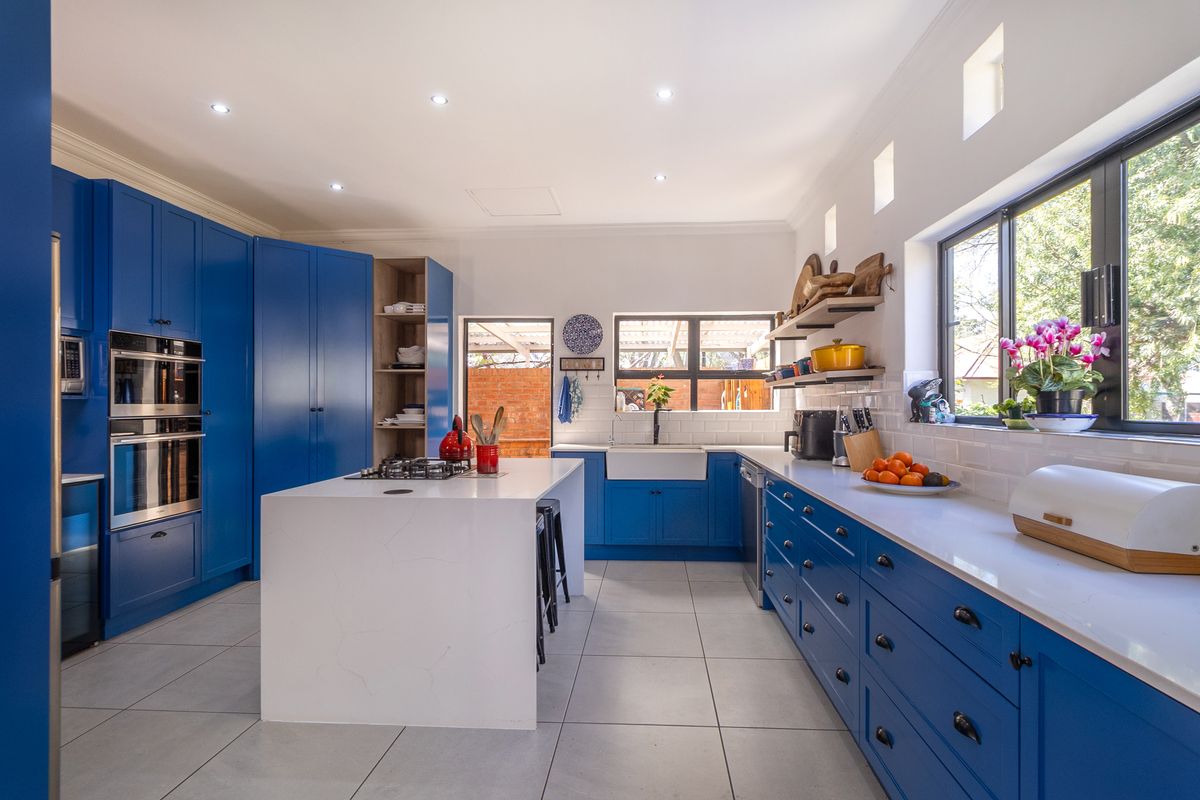 Modern kitchen featuring vibrant blue cabinetry, a central island with a gas cooktop, farmhouse sink, quartz countertops, and subway tile backsplash.