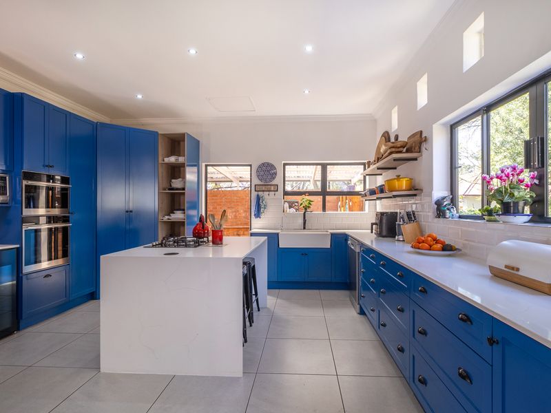 Modern kitchen featuring vibrant blue cabinetry, a central island with a gas cooktop, farmhouse sink, quartz countertops, and subway tile backsplash.
